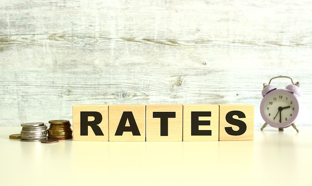 There are five wooden cubes with letters on the table next to the coins. RATES word. On a gray background.