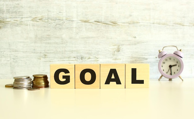 There are four wooden cubes with letters on the table next to the coins GOAL word On a gray background