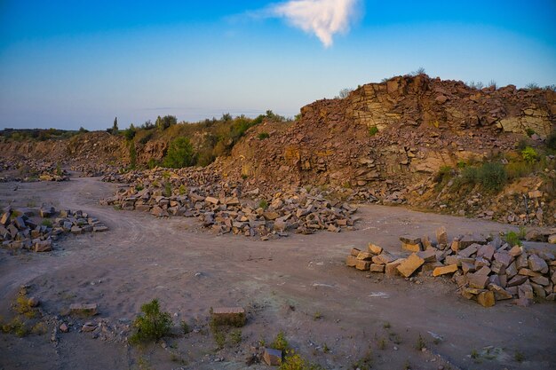 There are large piles of boulders in the warm evening light on the territory of old flooded stone quarry.