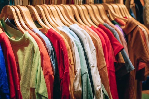 많은 다른 색깔의 옷이 상점의 옷걸이에 매달려 있습니다.
