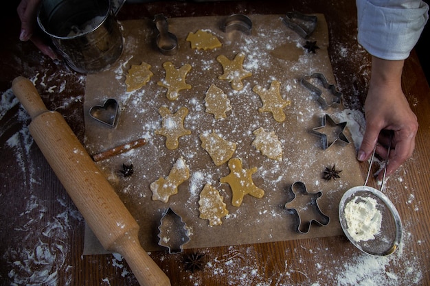 Ci sono biscotti già pronti di varie forme sulla carta da forno un mattarello tagliabiscotti a