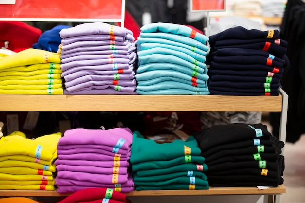 There are stacks of knitted sweaters folded longsleeves or Tshirts on a store shelf