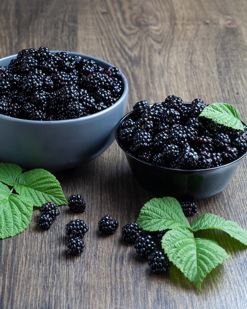 There are two plates of blackberries on the table. There are green leaves nearby.