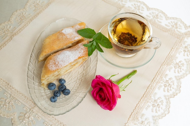 プレートにはアップルパイ ブルーベリーとミントの葉のスライスが 2 枚あり、その横には紅茶が置かれ、テーブルには生きたバラが飾られています。