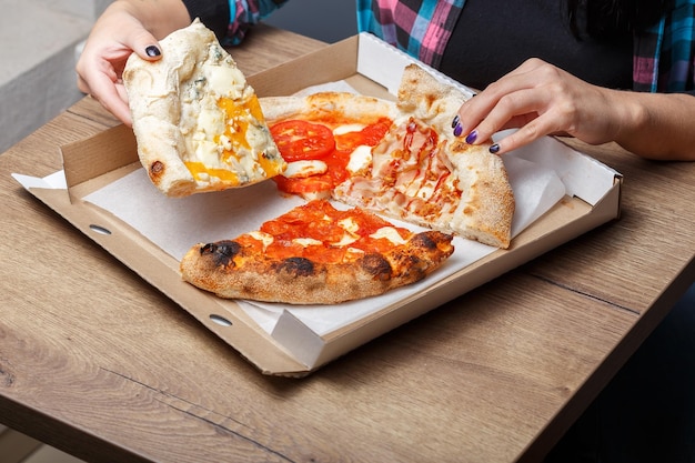 写真 テーブルの上にはさまざまな種類のピザとシャワルマが入った箱があり、女性の手が握られています。