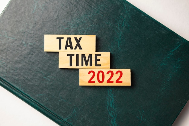 There is a blue notebook on a light gray background. Above are three wooden blocks with the words TAX TIME 2022