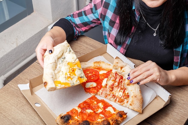 There is a box with different types of pizzas and shawarma on the table, women's hands are holding,