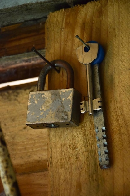 There is a bunch of different keys and a padlock on the wooden wall.