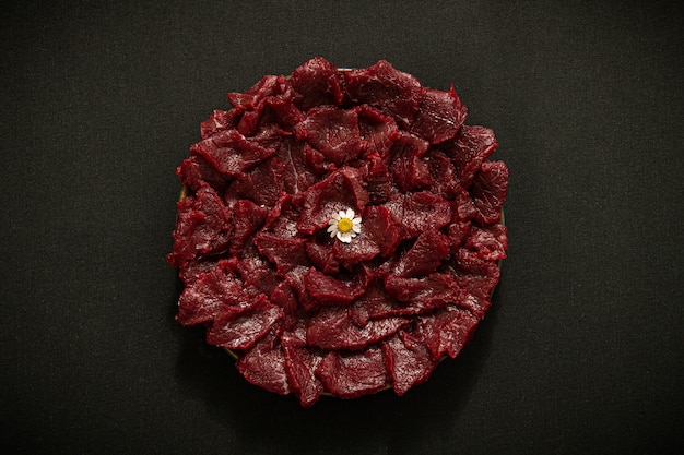 There is raw beef on a wooden plate The background is black texture