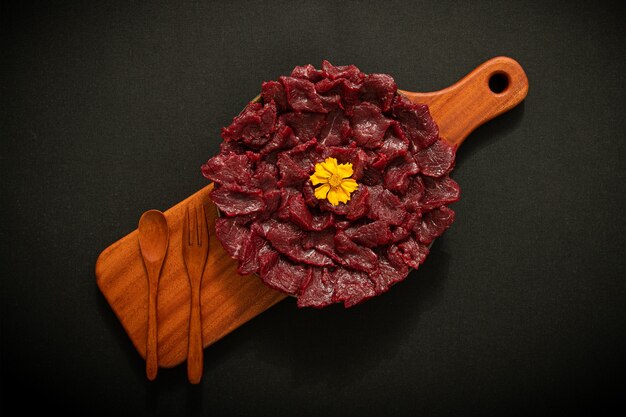 There is raw beef on a wooden plate The background is black texture