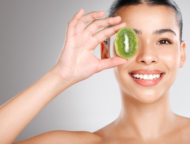 Theres no beauty like natural beauty Studio shot of an attractive young woman holding kiwi fruit to her face against a grey background