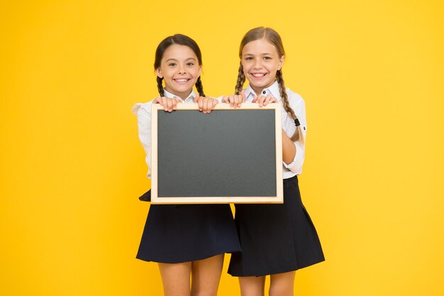 Theres place for your information Little kids holding blank blackboard for information on yellow background Small girls with tidy chalkboard for school information Information for you copy space