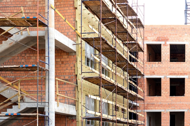 Thermal insulation of a red brick house with mineral wool. The use of scaffolding when building a house.