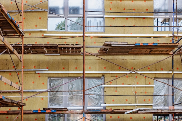 Thermal insulation of a red brick house with mineral wool. The use of scaffolding when building a house.