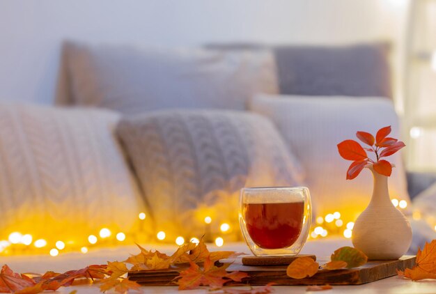 Thermo glass with hot tea in dark night room with autumnal
leaves