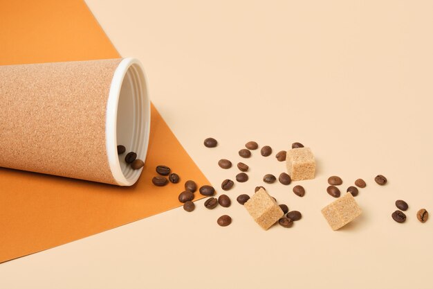 Thermo mug, scattered coffee beans and brown cane sugar cubes on brown and beige geometric background copy space