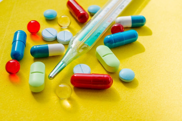 Thermometer en gekleurde pillen voor de behandeling van ziekten en verslavingthermometer farmaceutische medicijnkuur kleurrijke pillen en medicijnen in close-up verschillende tabletten op gele achtergrond Geneeskunde en gezond