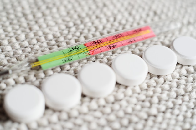 Thermometer and many colored tablets close-up on a knitted background