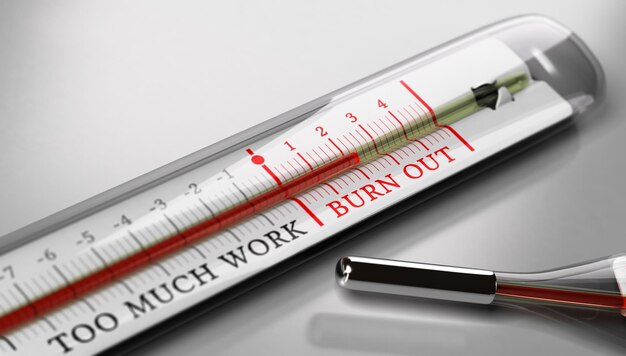 Thermometer met de tekst burn-out en te veel werk over grijze achtergrond. Concept afbeelding ter illustratie van beroepsmatige burn-out of werkstress.