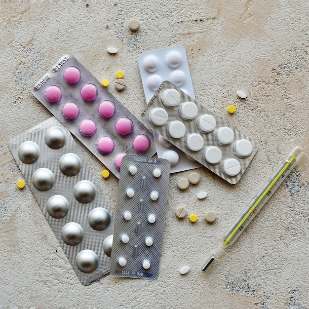 Thermometer and pill packs on a stone background. Top view.