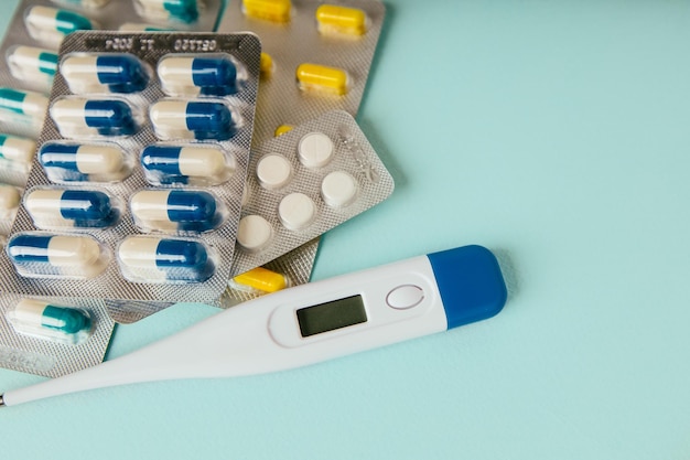 Thermometer pills and medical mask on blue background closeup Medicine and treatment