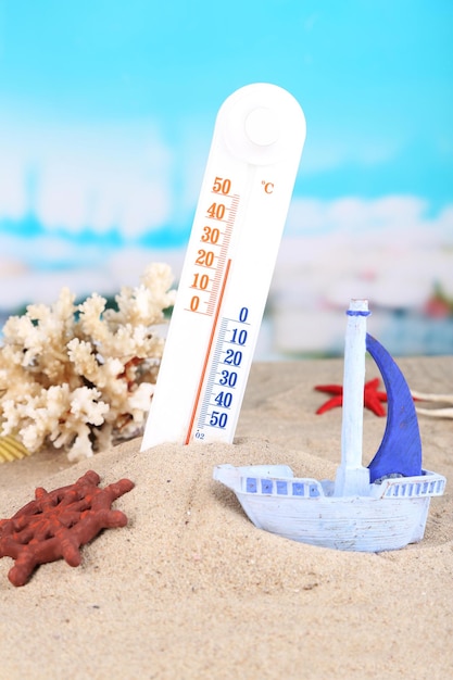 Thermometer in sand on bright background