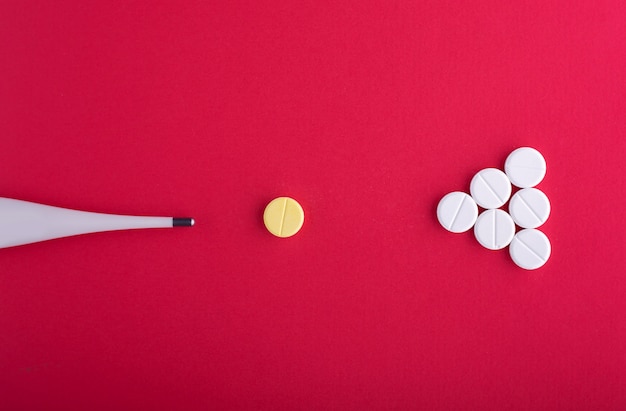 Thermometer and tablets on pink background