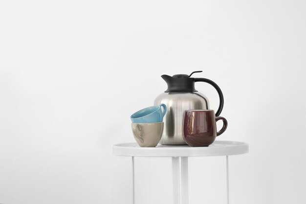 Thermos met koffie en bekers op tafel tegen de achtergrond van de muur