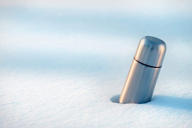 Thermos con caffè o tè in un cumulo di neve.