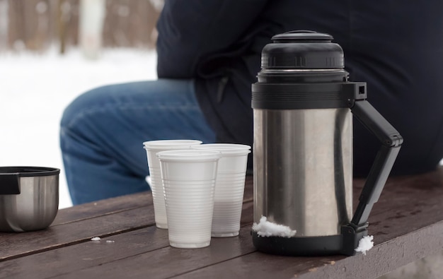 Thermos with cups on a bench in winter after a tea party in nature.
