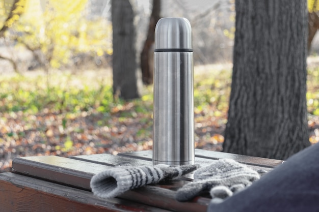 Thermos with hot tea or coffee on a bench in autumn park