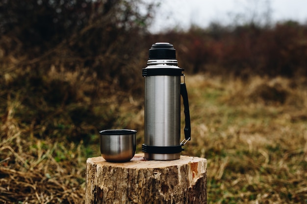 Thermosflessen die zich op houten login het bos bevinden. Ruimte voor tekst