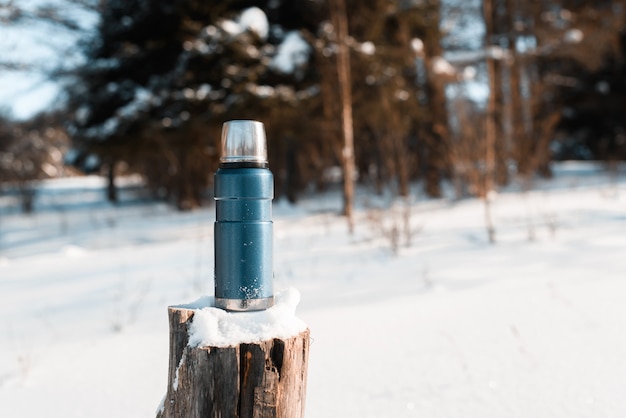 Thermosflessen staande op een besneeuwde stronk in een winterbos op een zonnige dag. Trekking concept, kamperen