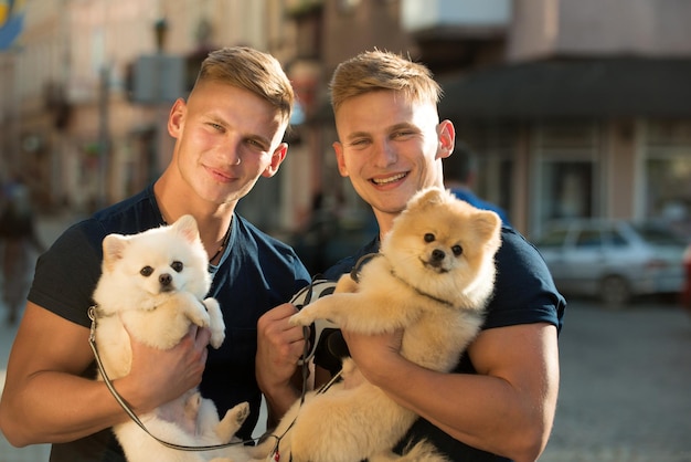 They belong together Happy family on walk Twins men hold pedigree dogs Muscular men with dog pets Happy twins with muscular look Spitz dogs love the company of their family