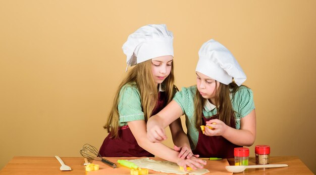 그들은 요리를 좋아합니다 사랑스러운 어린 소녀들은 함께 요리하는 것을 즐깁니다 요리 수업을 듣는 어린 아이들 요리 앞치마를 입은 귀여운 요리사 반죽으로 틀로 모양을 만드는 요리사