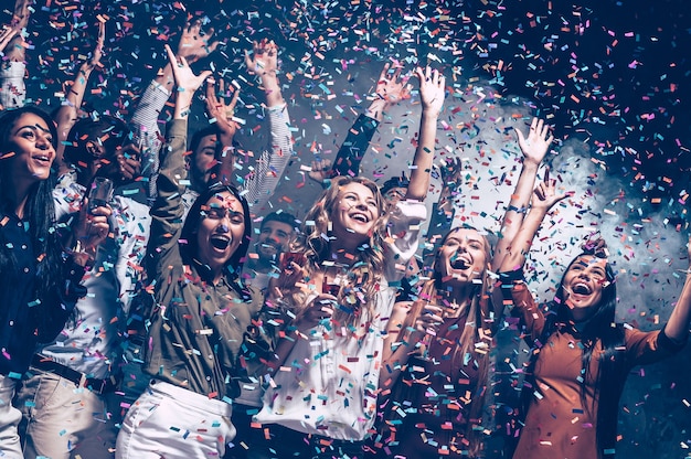 They love having fun. Group of beautiful young people throwing colorful confetti and looking happy