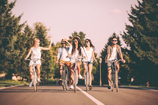 They love spending time together. Group of young people riding bicycles along a road and looking happy