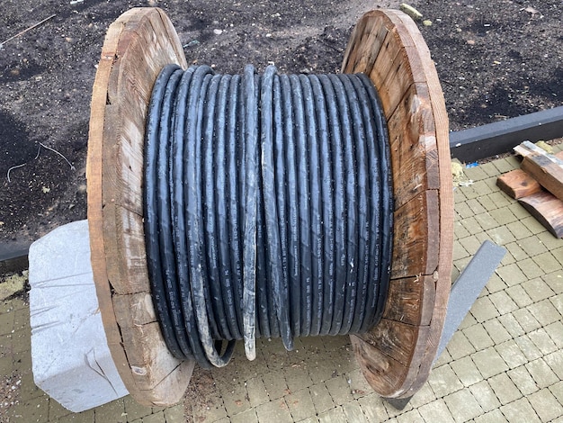 Толстый электрический черный кабель, свернутый в большой деревянный рулон, лежит на зеленом поле на Балтике.
