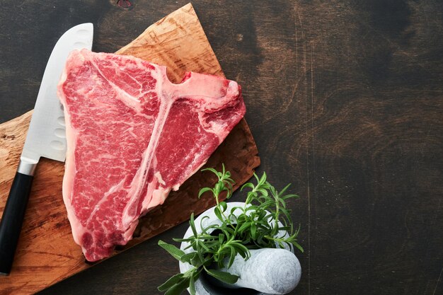 두꺼운 원시 TBone Steak Dryaged Raw Tbone 또는 porterhouse 쇠고기 고기 스테이크는 어두운 배경에서 허브와 소금을 곁들인 절단 멧돼지 상단 보기 및 복사 공간