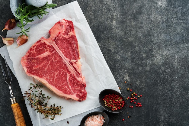 두꺼운 원시 TBone Steak Dryaged Raw Tbone 또는 porterhouse 쇠고기 고기 스테이크 양피지에 허브와 소금 어두운 배경 상위 뷰 및 복사 공간