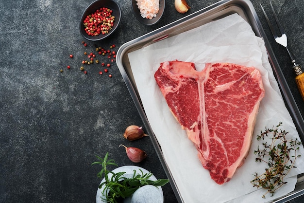 Thick Raw TBone Steak Dryaged Raw Tbone or porterhouse beef meat Steak on parchment paperwith herbs and salt on dark background Top view and copy space