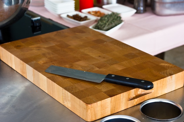 A thick wooden brown professional cutting board with a knife lying on it