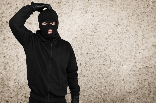 Thief in black balaclava and clothes on background