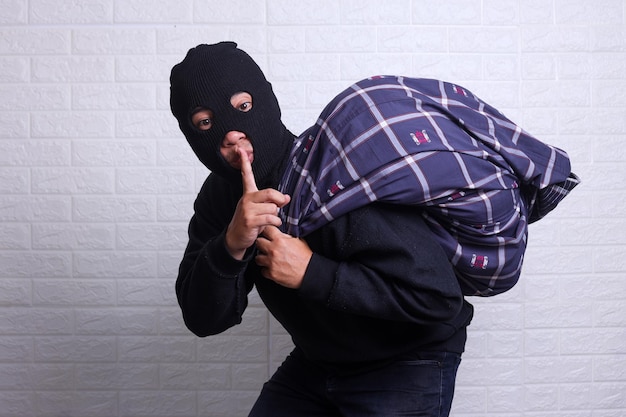 thief sneaking away with a bag while showing quiet hand gesture isolated on white background