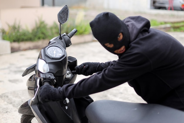 Вор в маске взламывает замок мотоцикла с помощью инструмента во время попытки преступления