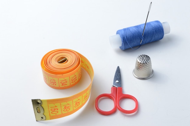 Thimble, needle with spool of thread, scissors and measuring tape .close-up.