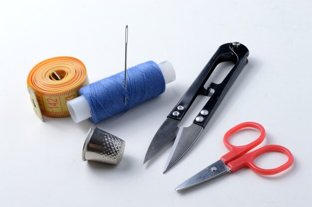 Thimble, needle with spool of thread, scissors and measuring tape on a white background .close-up.