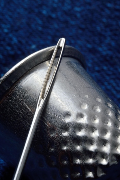 Thimble and sewing needle on blue material. close-up.