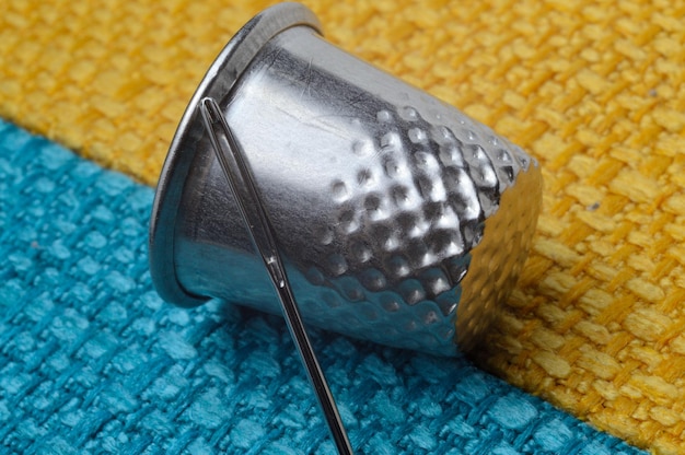 Thimble and sewing needle on yellowblue fabric closeup