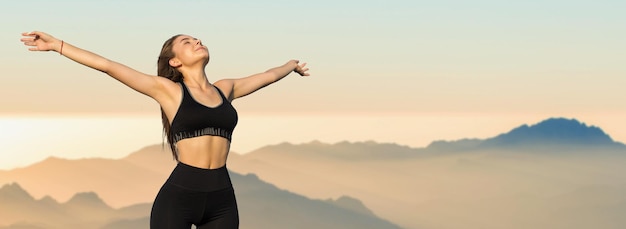 A thin athletic girl takes a break between classes on the background of mountains in the early morning enjoys silence and freedom